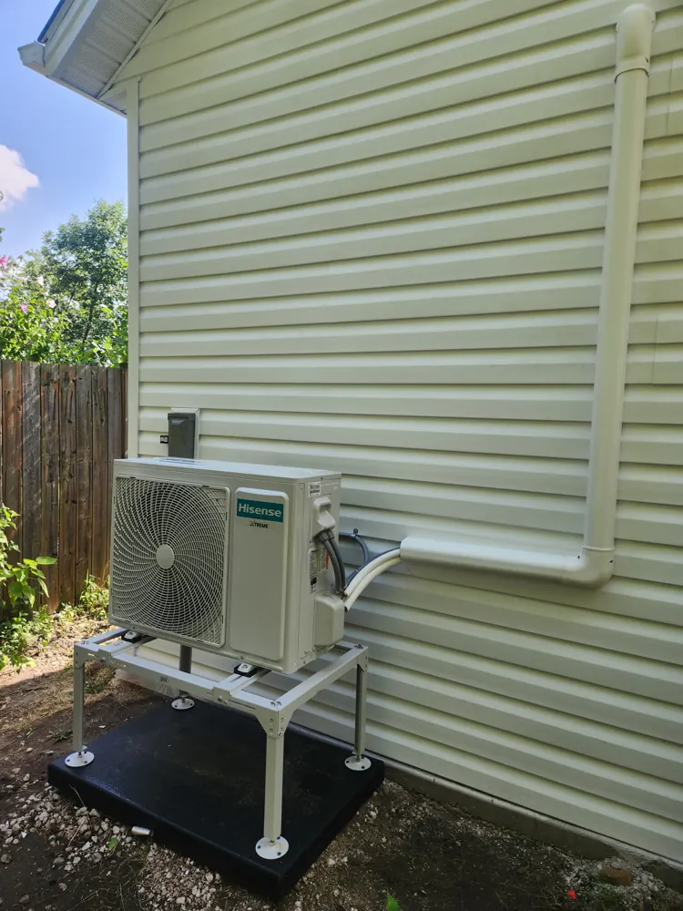 Mini split heat pump installed on a stand beside a home